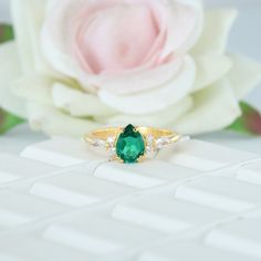 a green ring sitting on top of a table next to a white flower and pink rose