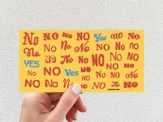 a hand holding up a yellow sticker with red and blue letters