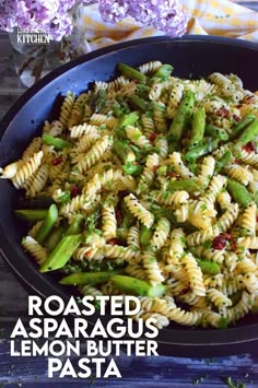 a bowl filled with pasta and asparagus on top of a table next to purple flowers