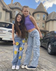 two girls standing next to each other in front of a house with smiley faces on their jeans