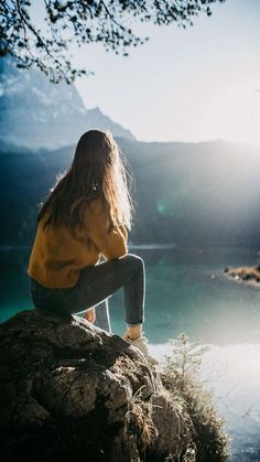 a woman sitting on top of a rock next to a lake