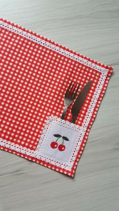 a red and white checkered placemat with cherries on it, next to a fork and knife