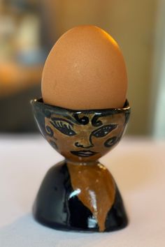 an egg sitting in a black and gold bowl on top of a table next to a white surface