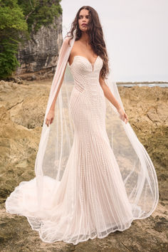 a woman in a wedding dress standing on the beach with her veil over her head