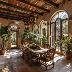 a dining room table with chairs and potted plants in the center, surrounded by arched windows