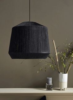 a black lamp hanging over a table next to a potted plant and vase with plants in it