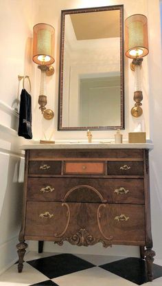 a bathroom with a checkered floor and an antique dresser in the corner, lighted by two lamps