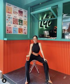 a woman sitting on a chair in front of an orange and green wall with posters behind her