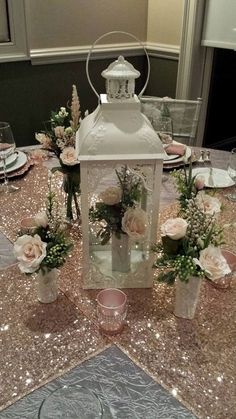 a white lantern on top of a table with pink flowers and greenery in vases