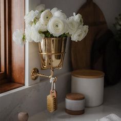 a gold vase with white flowers in it sitting on a bathroom counter next to a mirror