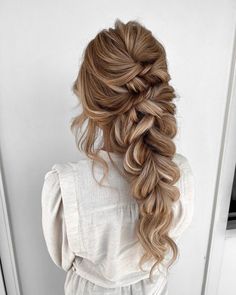 a woman with long hair in a half - up braid is standing against a door