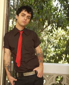 a man wearing a red tie standing next to a window with his hands in his pockets