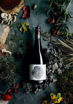 a bottle of wine sitting on top of a table filled with leaves and mushrooms next to other items