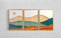 three wooden wall art pieces with mountains and the sun in the sky above them on a white brick wall