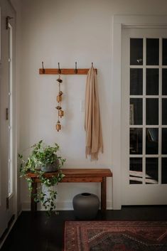 a wooden bench sitting in front of a white door next to a plant and coat rack