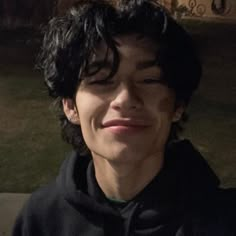 a young man with curly hair smiling and wearing a black hoodie in front of a building