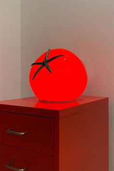 a tomato sitting on top of a red dresser next to a white wall and two drawers