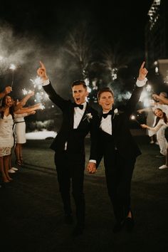 two men in tuxedos are holding sparklers and walking down the street at night