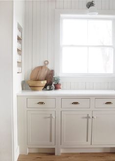 a kitchen with white cabinets and wooden flooring in front of a window that is open to the outside