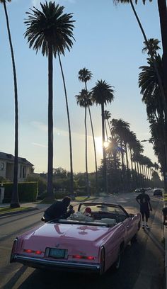 a pink convertible car driving down a street next to tall palm trees