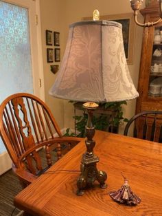 a table with a lamp on top of it next to a wooden chair and window