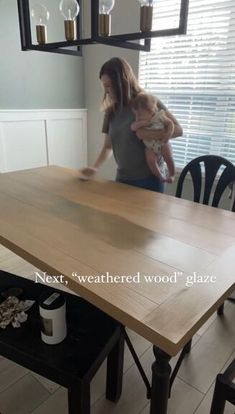 a woman holding a baby standing in front of a wooden table