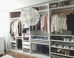 an organized closet with clothes, shoes and chandelier hanging from it's ceiling