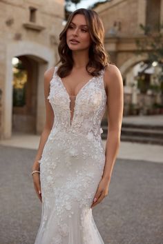 a woman in a white wedding dress standing on the street with her hands behind her back