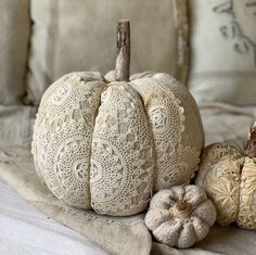 three decorative white pumpkins sitting on a bed next to pillows and pillow cases with lace