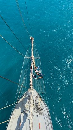 two people hanging out on the side of a sailboat in the middle of the ocean