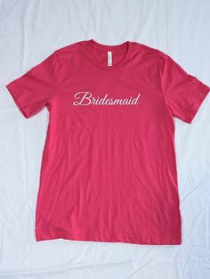 the bridesmaid t - shirt is pink and has white lettering on it that says,