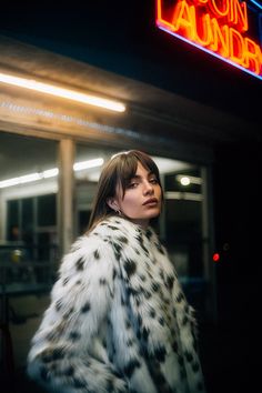 a woman in a white and black fur coat is standing on the street at night