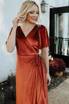 a woman wearing an orange dress and smiling at the camera with her hand on her hip