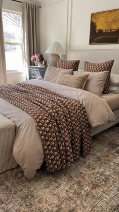 a bedroom with a large bed covered in brown and white sheets, pillows and blankets