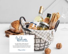 a basket filled with bread and wine on top of a white table next to a card