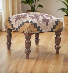 a wooden foot stool sitting on top of a hard wood floor next to a potted plant