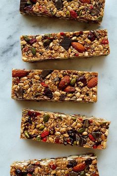 four granola bars lined up on top of a marble counter with nuts and seeds