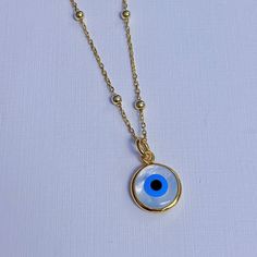 This necklace is made from a white mother of pearl slice cut into a round shape. The stone has blue and white enamel on the front to create an evil eye pendant. The stone is set inside a gold plated bezel. The charm hangs from gold plated satelite chain. Please choose the length you would like the necklace in. Please choose the chain style you would like your pendant on. Please note that all necklaces are handmade and may differ from the pictured. Absolutely EYE catching! A beautiful round mothe Handmade White Charm Necklace With Round Pendant, Handmade White Charm Necklaces With Round Pendant, White Handmade Round Charm Necklaces, White Charm Necklace With Pearl Pendant, White Round Handmade Charm Necklace, White Necklace With Charms And Round Pendant, Spiritual White Charm Necklace Nickel Free, White Amulet Style Medallion Necklace, White Charm Necklaces