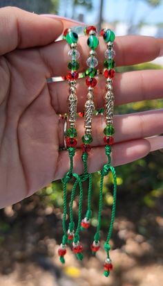 a hand holding three green and red beaded bracelets with bells on each end