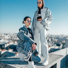 two women standing on top of a building with their arms around each other and looking off into the distance