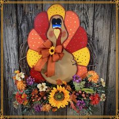 a turkey wreath with sunflowers and an orange bow hanging on a wooden fence