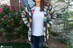 a woman standing in front of a house wearing a crocheted cardigan and jeans