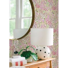 a table with a lamp, vase and books on it in front of a mirror