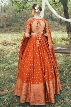 a woman in an orange and white dress is standing near a tree with her back turned to the camera