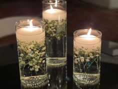 three glass vases with flowers and candles in them on top of a black table