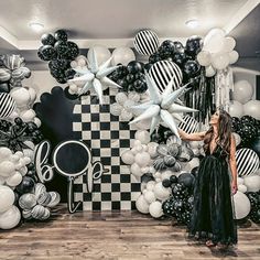 a woman is standing in front of balloons and black and white wall art at a party