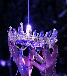 two hands holding up a crystal crown in the dark