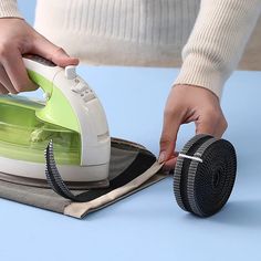 a person ironing fabric with a green and white steam iron on top of it