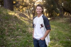 a young man standing in the woods with his hands in his pockets and smiling at the camera