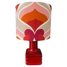 a red table lamp with a pink, orange and white shade on the top of it